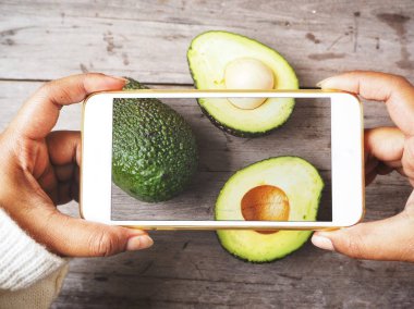 Kadın alarak fotoğraf smartphone ile ahşap arka plan üzerinde avokado