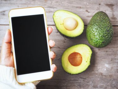 Yandan Smartphone ile ahşap arka plan üzerinde avokado 