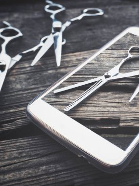 Fotoğrafta saç kesme makası ile smartphone üzerinde ahşap arka plan