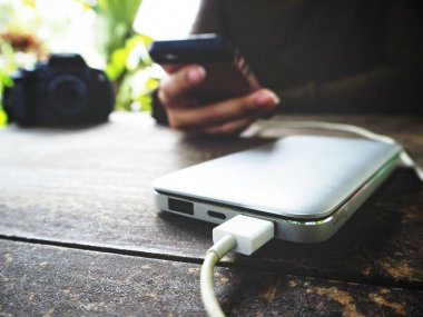 Ahşap masa üzerinde güç banka ile akıllı telefon kullanan kadın
