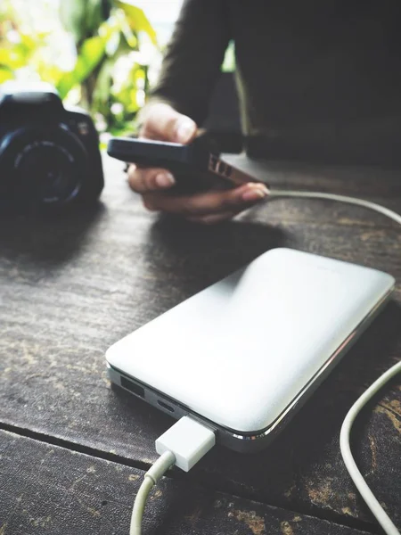 Ahşap masa üzerinde güç banka ile akıllı telefon kullanan kadın