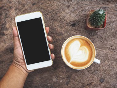 Kahve Kupası ahşap arka plan ile akıllı telefon kullanan kadın