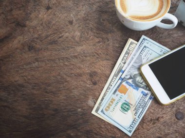 Dolar ile smartphone ve kahve Kupası ahşap arka plan üzerinde