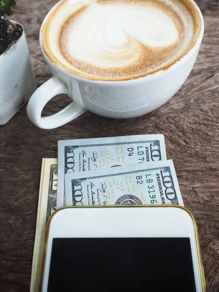 Δολάρια Smartphone Και Καφές Κύπελλο Φόντο Ξύλινη — Φωτογραφία Αρχείου
