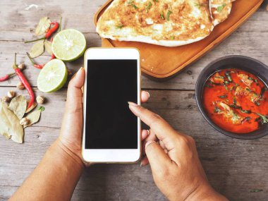 Hint naan ekmek ve köri ile ahşap masa üzerinde akıllı telefon kullanan kadın