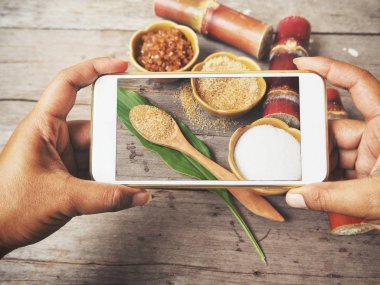 Ahşap arka plan üzerinde beyaz ve kahverengi şeker smartphone ile fotoğraf çekici