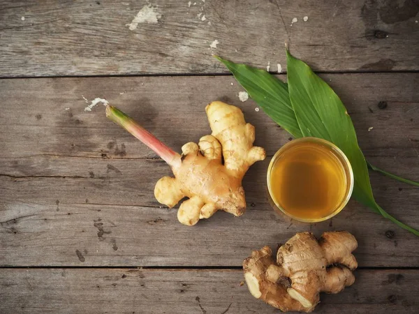 Ginger tea with ginger root and green leaves on wooden background