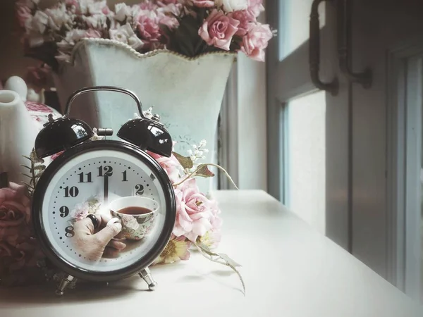 นาฬิกาปลุกที่มีถ้วยชาอยู่บนมือ — ภาพถ่ายสต็อก