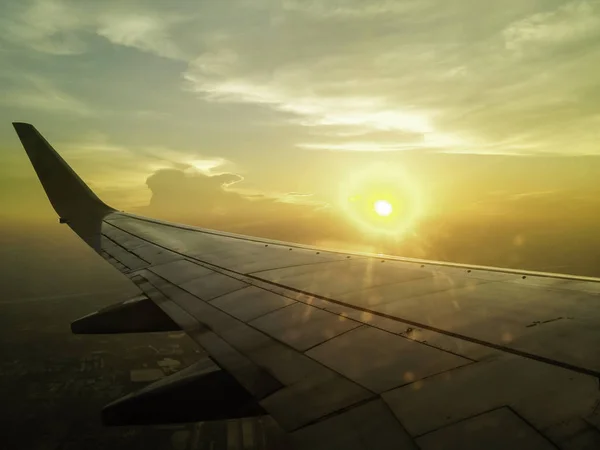 airplane wing in the sky with sun setting in background