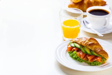 kruvasan sandviç somon ve avokado, kahve ve portakal suyu üzerinde beyaz bir arka plan ile