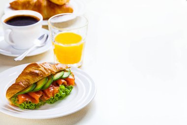 kruvasan sandviç somon ve avokado, kahve ve portakal suyu üzerinde beyaz bir arka plan ile