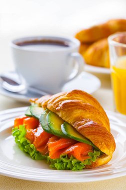 kruvasan sandviç somon ve avokado, kahve ve portakal suyu üzerinde beyaz bir arka plan ile