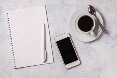 Gri bir arka plan üzerinde beyaz defter, kahve, telefon