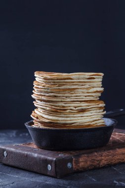 Dikey bir dökme demir tavada siyah bir zemin üzerine ballı krep