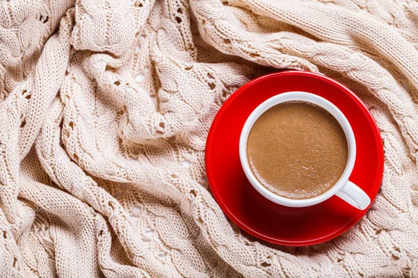Chocolate quente em uma xícara branca em uma placa vermelha em um cobertor quente de malha . — Fotografia de Stock