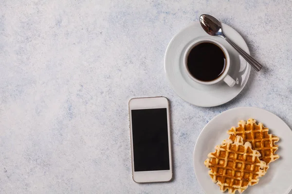 Schwarzer Kaffee in einer weißen Tasse mit belgischen Waffeln auf grauem Hintergrund, weißes Smartphone, Telefon, horizontal, Kopierraum — Stockfoto