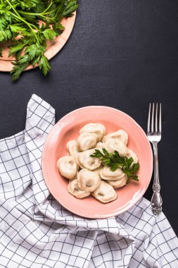 Dikey, düz siyah arka plan, maydanoz, pembe bir tabağa haşlanmış köfte yatıyordu