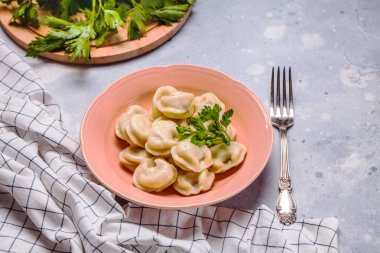 Bir gri arka plan, maydanoz, yatay pembe bir tabağa haşlanmış köfte