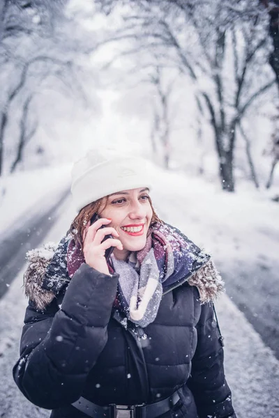 Pretty woman talks with mobile phone in snowy landscape.