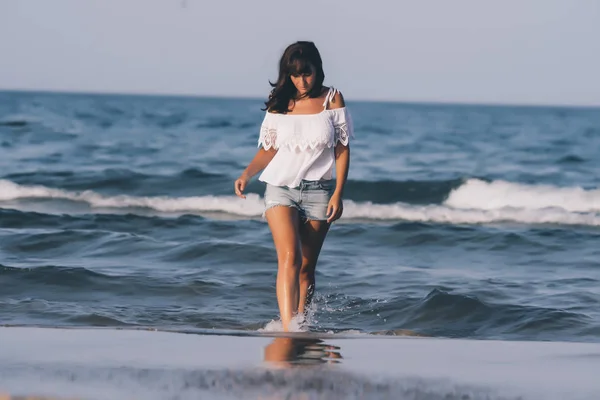 Pretty woman with short jeans getting wet in the beach water.