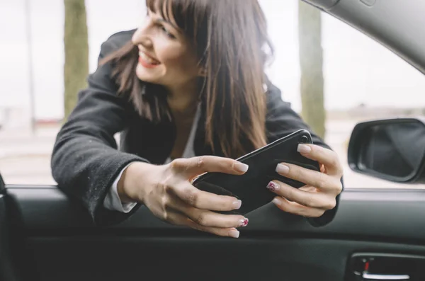 Executive brunette woman in car window with mobile phone.