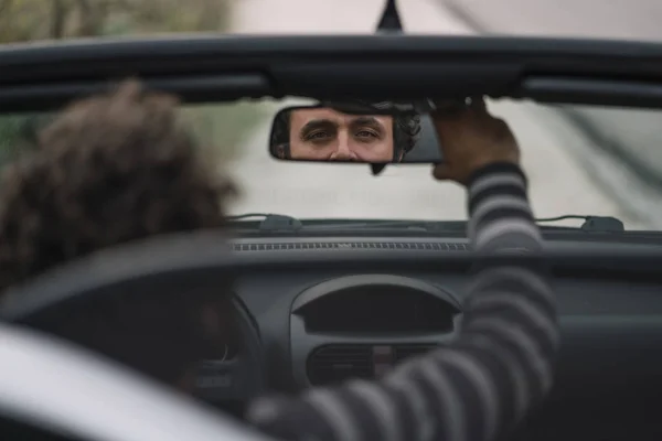 Man inside convertible car placed rear view mirror.