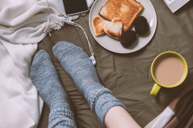 Kadın yatakta tost, telefon ve kulaklık ile bir kahve içme
