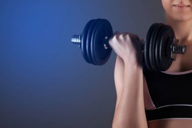 Sportif bir kız bir dumbbell onun elinde tutan, bir kas sallıyor. Karanlık bir arka plan karşı