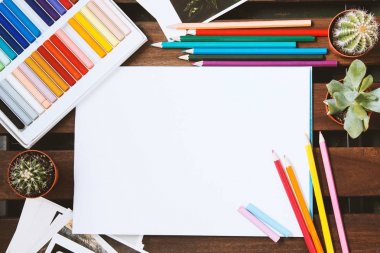 kalemler ve pastel karanlık bir masaya yayılmış. Metin için beyaz boş sayfa