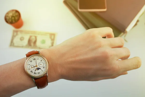 business woman looks at the watch on her wrist, over a white table on which money and diaries lie