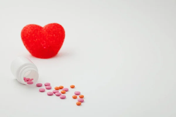 Pillen gegoten uit een fles en hart op een witte achtergrond — Stockfoto