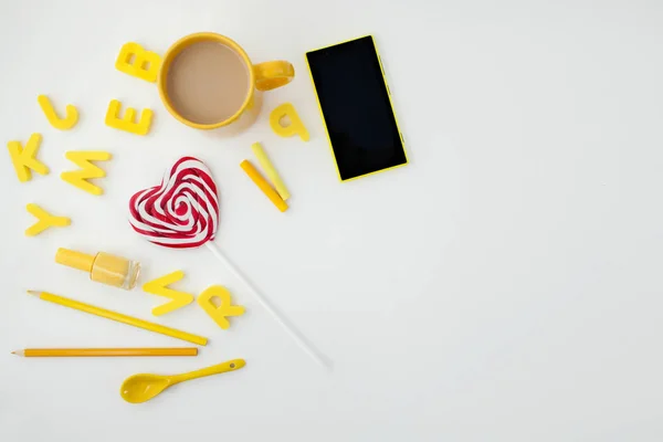 Gele kopje, hart vormige snoep, letters, gele telefoon en potloden op witte achtergrond. Plek voor tekst. Van bovenaf bekijken — Stockfoto