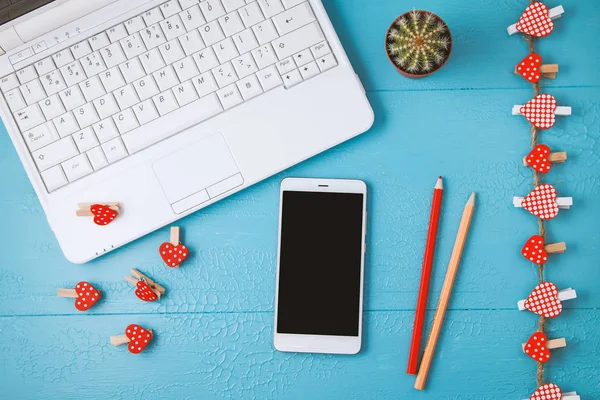 workplace on a blue laptop background, smartphone and red decorative hearts, pencils. Valentine day, holiday background