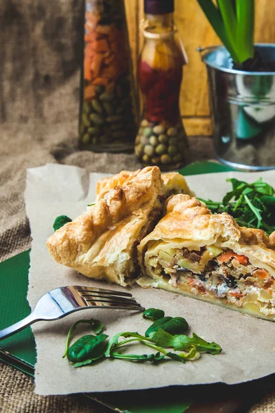 puff pastry stuffed with meat, carrots, potato pie, decorated with rucola, on a dark background Background for postcard. Menu, restaurant, recipe concept, served in. Rustik stile