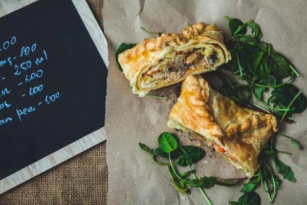 puff pastry stuffed with meat, carrots, potato pie, decorated with rucola, on a dark background Background for postcard. Menu, restaurant, recipe concept, served in. Rustik stile