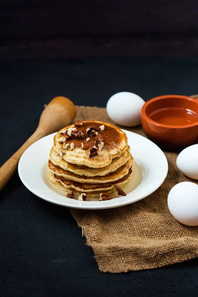 Appetitliche Pfannkuchen mit Honig und Nüssen auf einem dunklen Tisch mit Eiern und einer Schüssel Honig Menü, Restaurant Rezeptkonzept. serviert in — Stockfoto