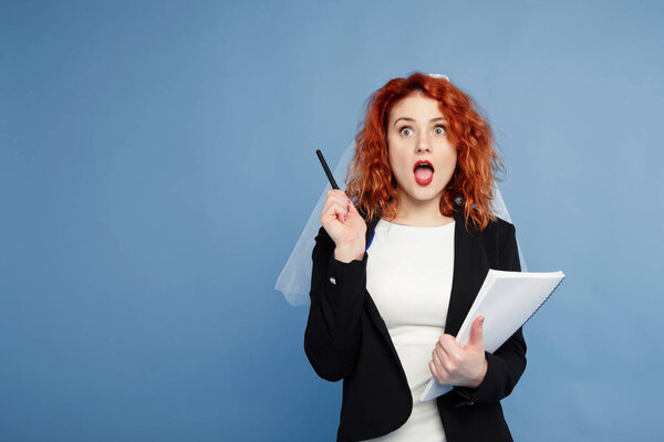 red-haired girl, the bride is holding a notebook for notes with a pensive look, planning her business. Isolate on a blue background, place for text. concept for the organizers of wedding celebrations.