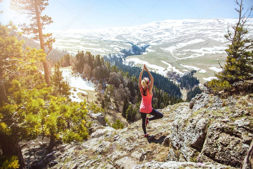 young girl traveler sits on top of a mountain in a yoga pose. The girl loves to travel. Concept for travelers. View from back of the tourist traveler on background mountain