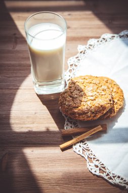 Bir bardak süt ve kurabiye güneş ışığı altında ahşap bir zemin üzerine. Menü ve Restoran kavramı