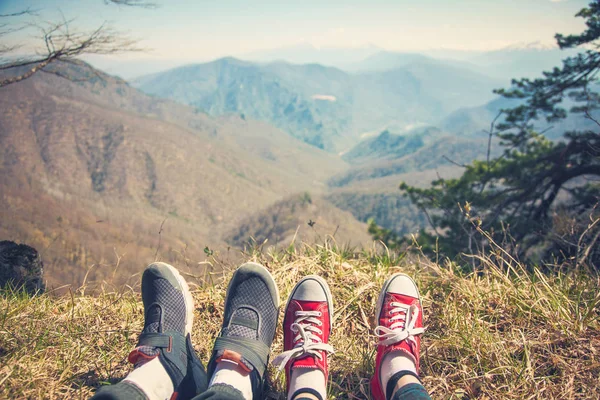 foot girl and guy traveler who sits atop a mountain and looks at a mountain plateau View from back of the tourist traveler on background mountain