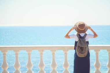 Genç ve güzel kadın turist güneşli bir günde deniz kıyısında güzel bir mesafe görünüyor. Gelen turist Gezgin arkasında görüntülemek