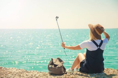 Genç ve güzel kadın turist selfie portre fotoğrafı için seyahat etmek blog kız çeker güneşli bir deniz kıyısı alır. Gelen turist Gezgin arkasında görüntülemek.