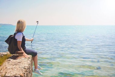 Genç ve güzel kadın turist selfie portre fotoğrafı için seyahat etmek blog kız çeker güneşli bir deniz kıyısı alır. Gelen turist Gezgin arkasında görüntülemek