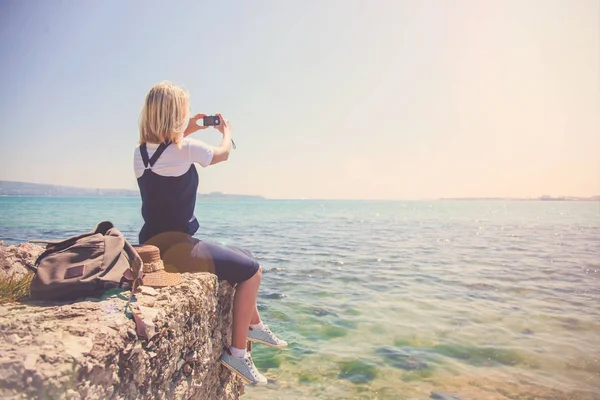 Jeune fille voyageur prend des photos sur l'appareil photo belle vue de la mer. La fille adore voyager. Concept pour les voyageurs. Vue de dos du voyageur touristique sur fond mer — Photo