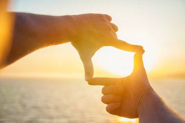 Eller streç denizin üzerinde güneşin doğru mans. Katlanmış parmaklarımın arasından günbatımında bir adam görünüyor.