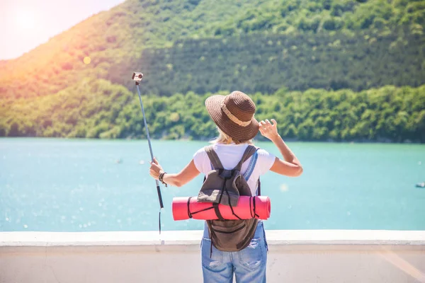 Kız gezgin bir dağ Gölü üzerinde bir eylem kamera ile selfi yapar. Bir fotoğraf için seyahat etmek blog yapıyor. Gelen turist Gezgin arkasında görüntülemek