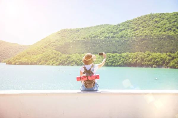 Kız gezgin bir dağ gölü kızı smartphone ile fotoğraf için seyahat etmek blog görünümünden turist Gezgin geri alır