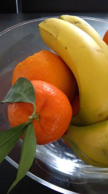 Siyah arka plan üzerine cam kaseye mandalina, portakal ve muz yakın çekim