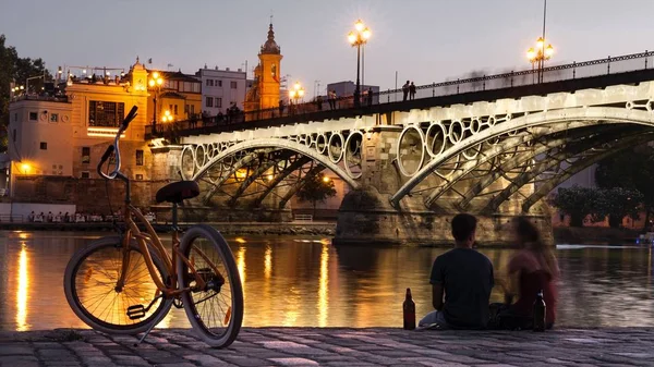 Akşam sahne çift ve Bisiklet arka planını Triana Köprüsü, Sevilla ile