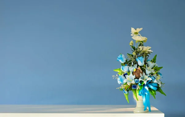 Bukett konstgjorda blommor vas på elfenben tabell med blå vägg — Stockfoto
